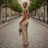 Woman in a beige sleeveless jumpsuit stands on a cobblestone city street, holding a small brown handbag and looking over her shoulder.